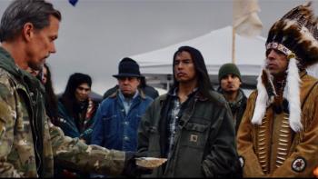On Sacred Ground Movie: A White man in Army fatigues holds out an offering to a First Nation chief and other Native American men
