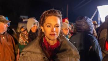 On Sacred Ground Move: A Native American woman looks forward with a hopeful smile in front of a mass of people in coats standing outside