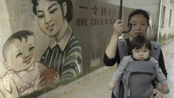 One Child Nation Movie: A mother holds her baby in a carrier in front of a mural that reads "One child is best"