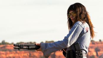 Onslaught Movie: Wearing shaded glasses, Celeste holds a high-powered rifle as she shoots targets in the desert