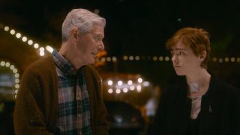 The Optimist Movie: Standing outside at night, lights visible in the background, Herbert and Abby talk