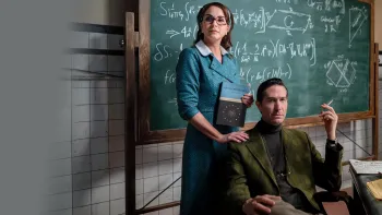 Our Times movie: Mexican woman center in teacher outfit stands in front of chalkboard with math equations and next to Mexican man sitting in chair