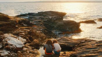 Over/Under: Two girls sitting on coastal rocks, watching the sunset over the ocean