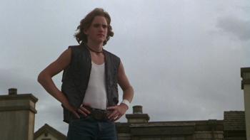 Over the Edge: Young man in sleeveless shirt stands with his hands on his hips and his shoulder-length hair blowing in the wind