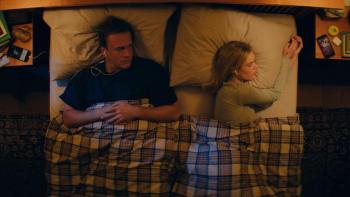 Over Your Dead Body movie: Jason Segel and Samara Weaving lie in bed, facing opposite directions, under a plaid blanket