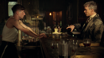 Barry Keoghan and Cillian Murphy face each other across a dimly lit bar in a tense scene from Peaky Blinders: The Immortal Man