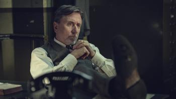 A man in a waistcoat and shirt sits pensively at a desk in a dimly-lit office in Peaky Blinders: The Immortal Man