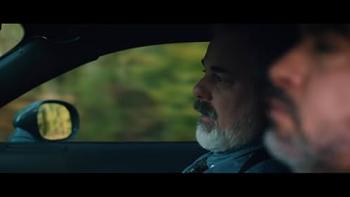 Porch Pirates movie: Side-view of the driver's side of a car shows a Latino American man right and a White man in the passenger seat