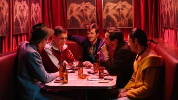 Postcards from London: Harris Dickinson wears a sports top and sits in a bright red booth with four men in colorful suits