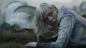 Predator: Badlands Movie: Thia (Elle Fanning) crawls on the ground, a spaceship in the background