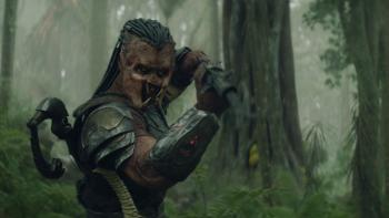 Predator: Badlands Movie: On a misty green forest planet, Dek holds his weapon at the ready