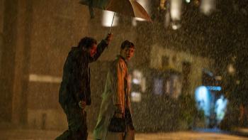 John Magaro holds an umbrella over the head of Britt Lower as they walk through the pouring rain