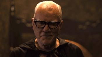 Psycho Killer Movie: Satanic priest Mr. Pendleton (Malcolm McDowell), a cape tied around his neck, looks straight ahead