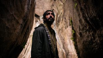 Rabbit Trap: Dev Patel stands in between two rock faces, light illuminating him from behind