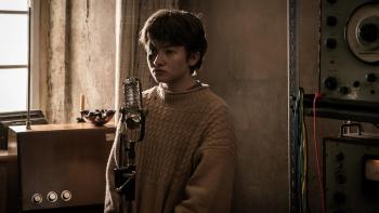 Rabbit Trap: A child stands in front of a microphone in a dimly-lit room, looking serious