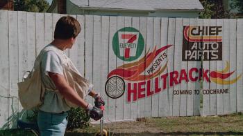 Rad movie: Bill Allen stands over his bike looking at painted ad on a fence for Helltrack