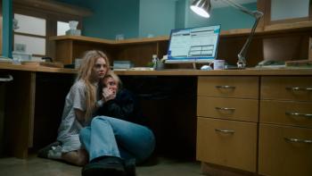 Ready or Not 2: Here I Come movie: Grace and Faith crouch behind a desk, terrified and handcuffed together