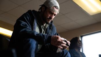 Red Right Hand Movie: Wearing a coat and a backward baseball cap, Cash (Orlando Bloom) sits in a chair and examines something he holds in his hands, his face deep in concentration