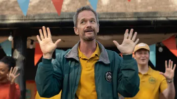 Sunny Dancer: Man in green jacket raising hands, with festive bunting and smiling people in the background