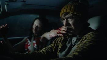 Resident Evil Movie: A woman in a passenger seat reaches a bloody hand in front of Bryan's faces as he drives