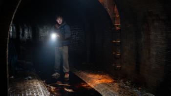 Resident Evil Movie: In a sewer with blood on the floor, Bryan holds a flashlight and reacts to something odd