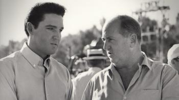 Return of the King: A black and white still of Elvis standing outdoors talking intently with his manager, Colonel Tom Parker.