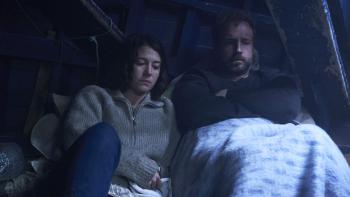 Rich Flu: A man and woman sitting close together under a blanket, appearing thoughtful and somber
