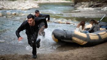 River Wild movie: Two women sit in beached raft on right while a white man chases a white man in shallow water to the left of raft