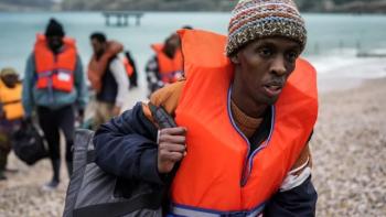 Run: Group wearing life jackets walks on a pebble beach, carrying bags