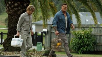 Runner movie: Alan Ritchson, holding a birdcage, walks next to Owen Wilson, holding a cooler