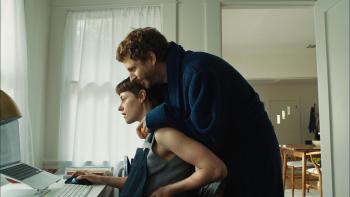 Sacramento movie: Michael Cera cuddles Kristen Stewart while she's sitting at a desk looking at a computer monitor