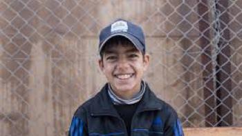  Salam Neighbor: Smiling boy with baseball hat in front of barbed wire fence