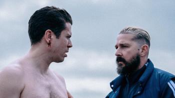 Salvable: Two men face each other tensely; one is shirtless with blood on his ear, the other wears a tracksuit and looks stern