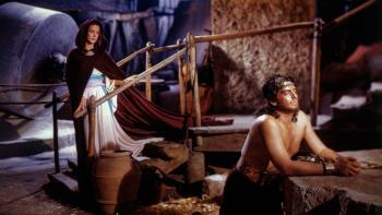 Samson and Delilah: A shirtless muscular man kneels at a rock and a woman in a cloak stands behind him