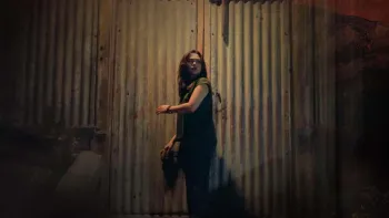 Scarecrow movie: Filipino woman with long black hair in sleeveless green shirt, center, looks behind her before going into a large farm shed