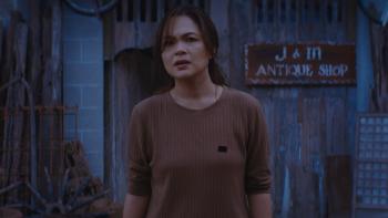 Scarecrow movie: Filipino woman with black hair tied back, in light brown shirt, stands outside an old antiques shop shack