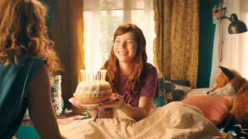 School of Magical Animals 2: A teen girl with red hair smiles as she gets a birthday cake in bed