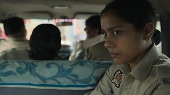 Santosh: An Indian female police officer sits in the back of a vehicle with a serious look on her face 