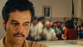 The Secret Agent movie: Wagner Moura looks concerned in an office, with his back turned to a crowd of people
