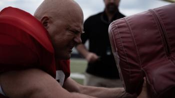 The Senior Movie: In uniform, Mike strains against a blocking dummy with all his might