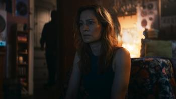 Shelby Oaks Movie: Mia (Camille Sullivan) seems to be watching something on TV while a dark figure lurks behind her