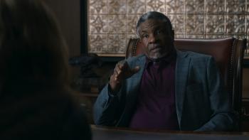Shelby Oaks Movie: A prison warden (Keith David) in a suit speaks to Mia from behind a desk