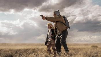 She Rides Shotgun Movie: Among the scrub brush and under a cloudy sky, Polly stands with Nathan, who aims a gun