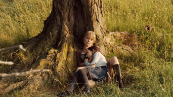 Silent Hill movie: A blonde woman lies against a tree trunk cradling young girl outdoors