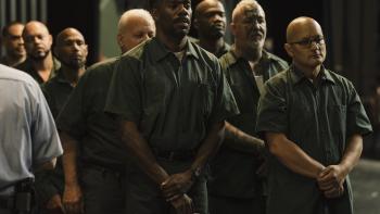 Sing Sing Movie: Divine G and Mike Mike stand somberly with several other men, their hands clasped in front of them