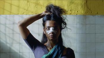 Sister Midnight: An Indian woman with bandages on her nose, holds her hair above her head with her right hand