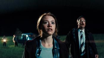 Watch the Skies: A White teenage girl and an older White mustached man look up toward the sky, a van with other people just behind them