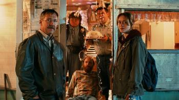 Watch the Skies: An older White mustached man and a White teenage girl stand either side of the door to a motorhome, three people inside holding cake