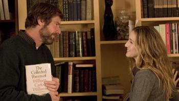 Dennis Quaid stands in front of a bookcase, holding a book under his arm and smiling at Sarah Jessica Parker.