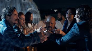 Solo Mio movie: Kevin James is in the center of a group of people doing shots at a rooftop bar